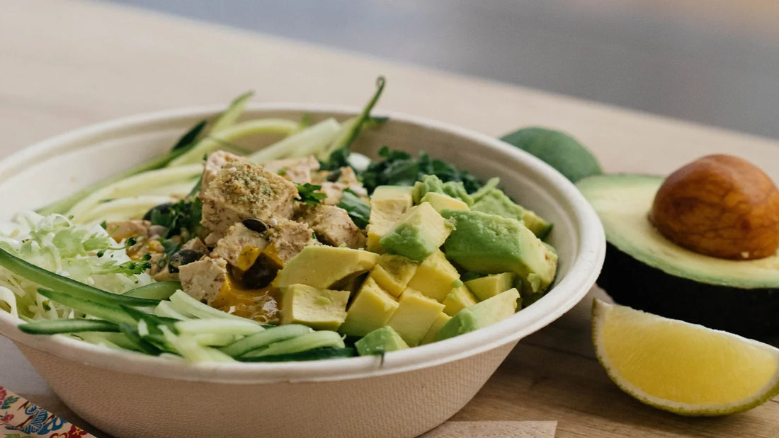 A bowl of avocado, cucumber and leafy greens beside half an avocado.